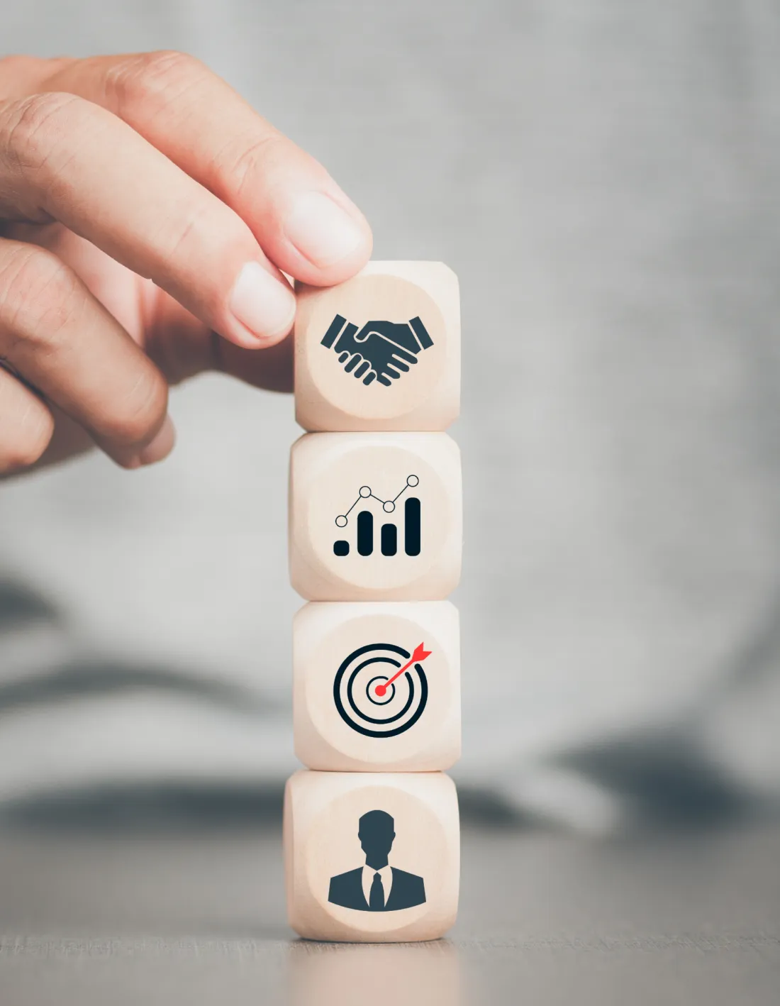 A hand stacking wooden blocks marked with partnership, growth, target and people icons
